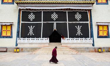 Monk in red robes walking past the gate of Songzanlin Monastery in Shangri-La，yunnan