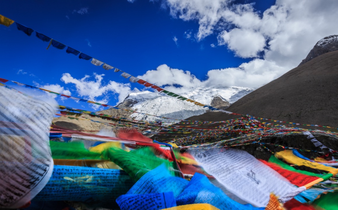 Gyatso La Pass in Tibet with prayer flags under blue sky and clouds
